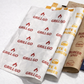 Four branded paper food bags arranged overlapping on a light gray background. The bags are white, tan, and navy blue, each printed repeatedly with the restaurant name and logo in red, yellow, and white respectively.