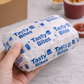 Hand holding a wrapped food item labeled 'Tasty Bites' with a blurred background of food containers.